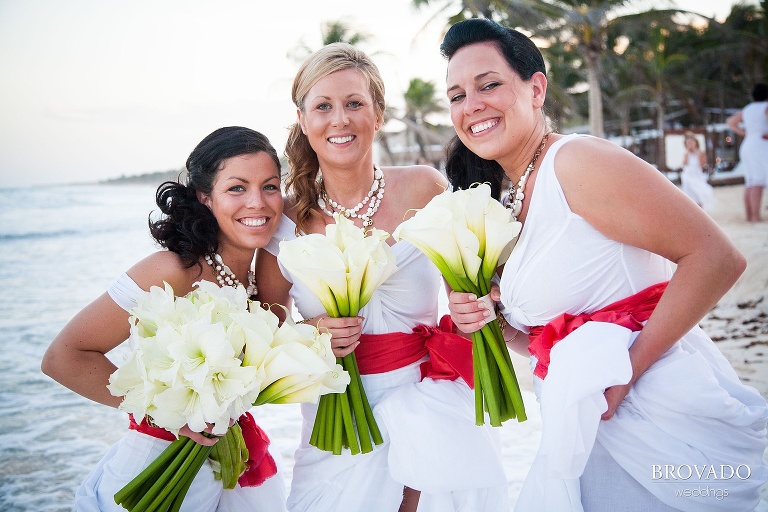 bridesmaids hold lily bouquets and pose on the beach