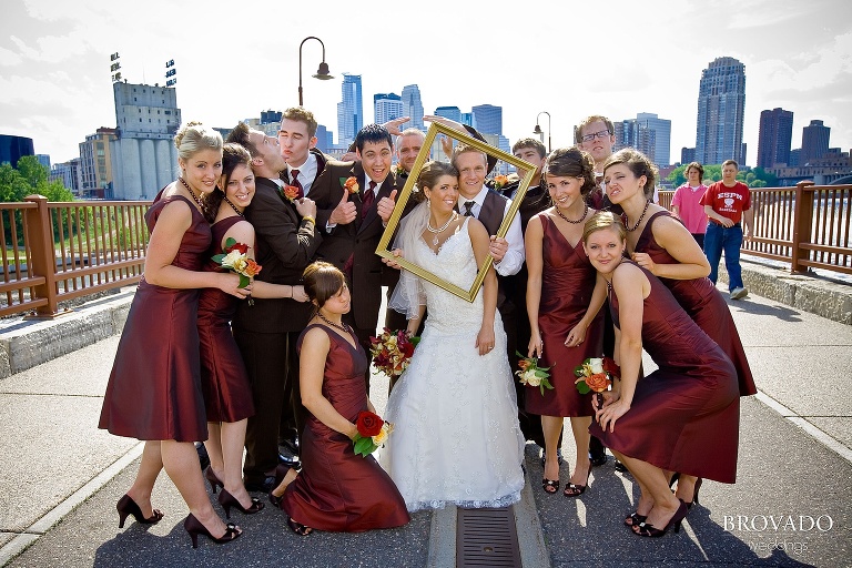 wedding party poses with a picture frame on stone arch bridge