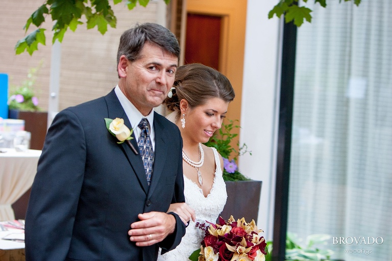 father of the bride smirking at the camera while walking the bride down the aisle