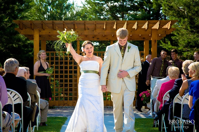 bride and groom cheer while walking down aisle