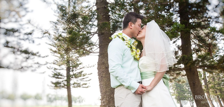 bride and groom kissing in front of evergreens