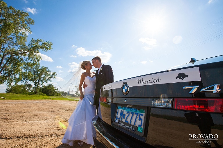 bride and groom standing by a car that says just married