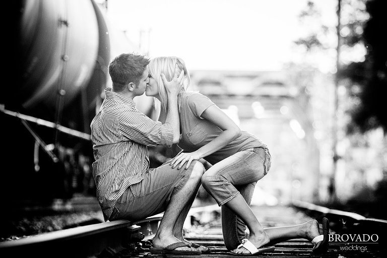 black and white engagement photography of couple kissing on railroad tracks
