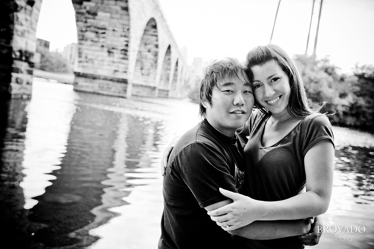 engaged couple embracing in front of mississippi river and stone arch bridge