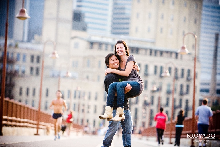 man holding his fiance in front of minneapolis skyline on stone arch bridge