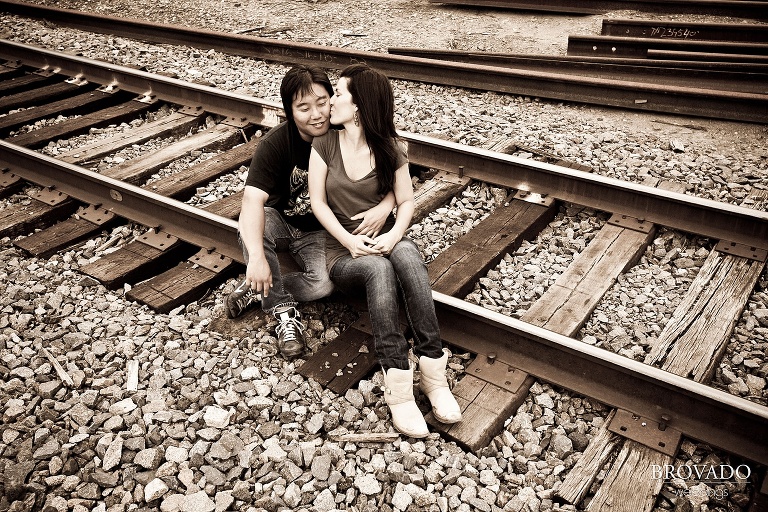 woman kissing fiance on the cheek while sitting on train tracks