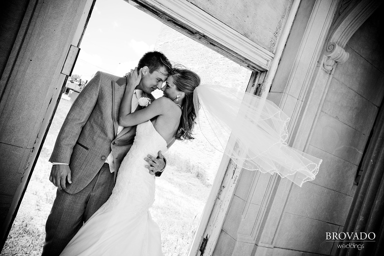 black and white photograph of bride and groom embracing while the veil blows in the wind