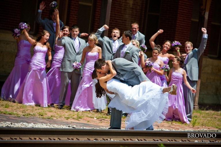 wedding party cheering behind a kissing bride and groom