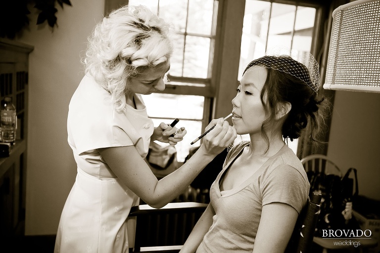 sepia photograph of bride getting her lipstick done while wearing mesh veil