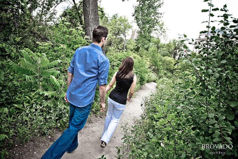 woman leading her fiance down a wooded path during engagement photographs