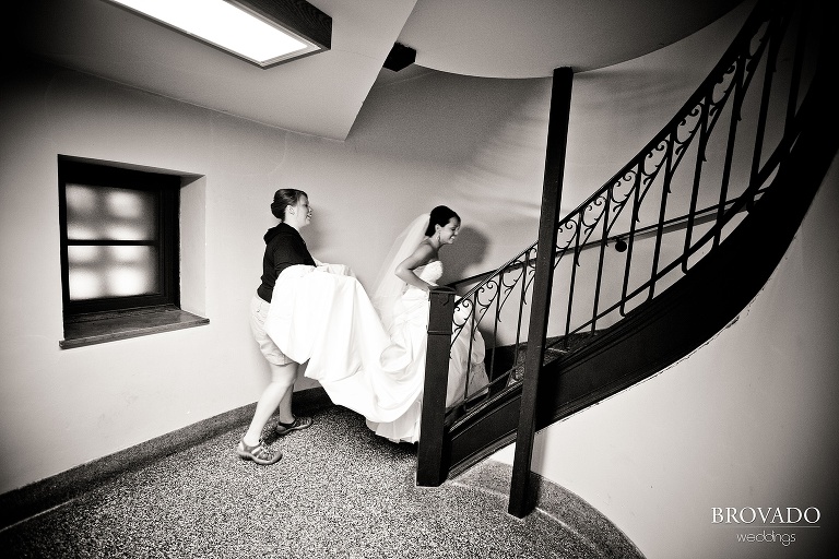 bride getting help walking up spiral staircase in large white wedding dress