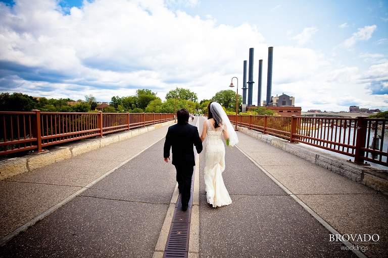 high contrast photograph of bride and groom walking down stone arch bridge