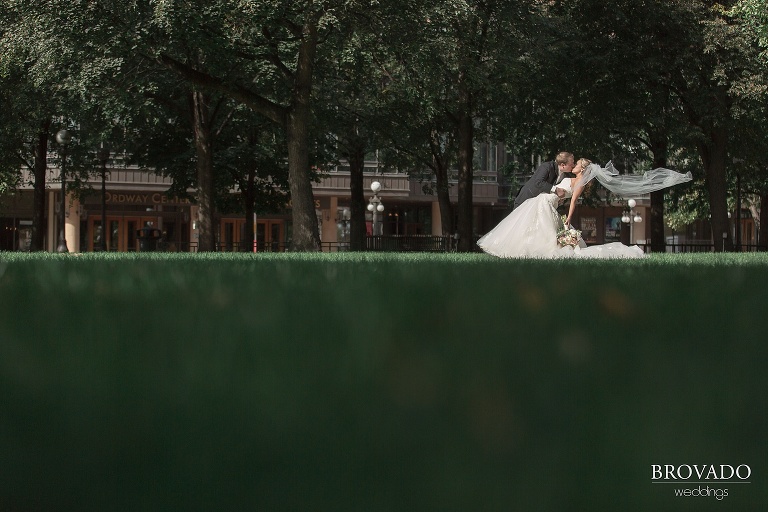 Grooms dips and kisses bride while her veil flies in the wind