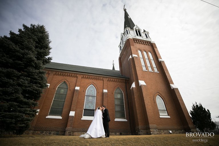Wide angle of Heidi and Tony kissing by church