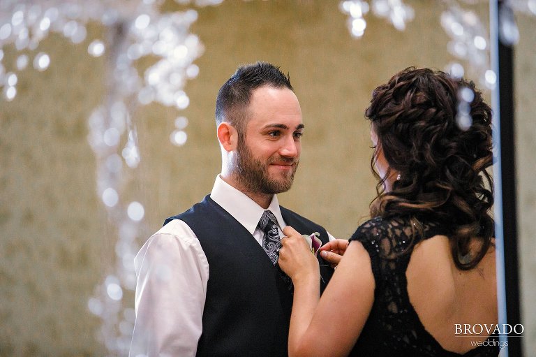 Bridesmaid putting on groomsman's boutonniere 