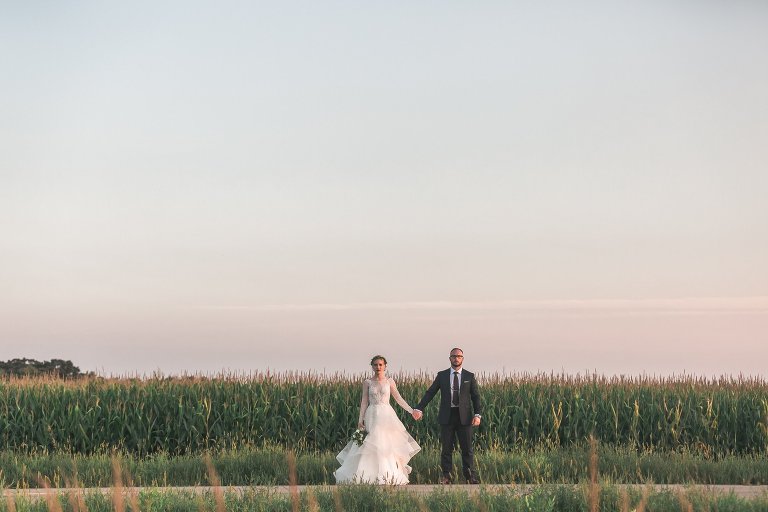 Zach and Coty holding hands in front of corn field at sunset