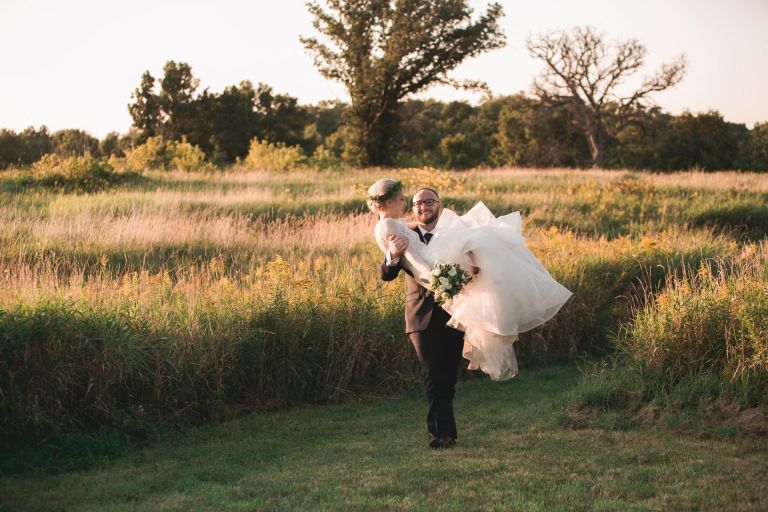 Zach carrying his bride through a field at sunset