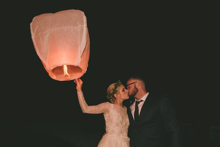 Bride and groom kiss while lighting paper lantern