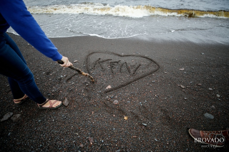 Brides writing their initials in the sand of lake superior