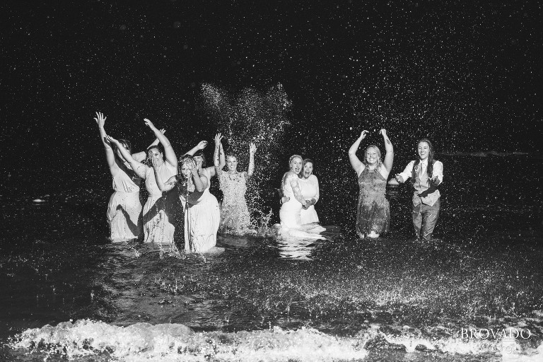 Same sex couple and wedding party splashing in lake superior