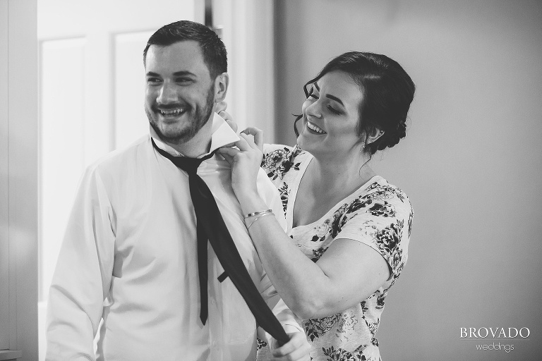 Bridesmaid helping groomsman put on his tie in black and white