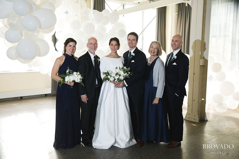 Bride and groom posing with family in front of girl friday balloon installation