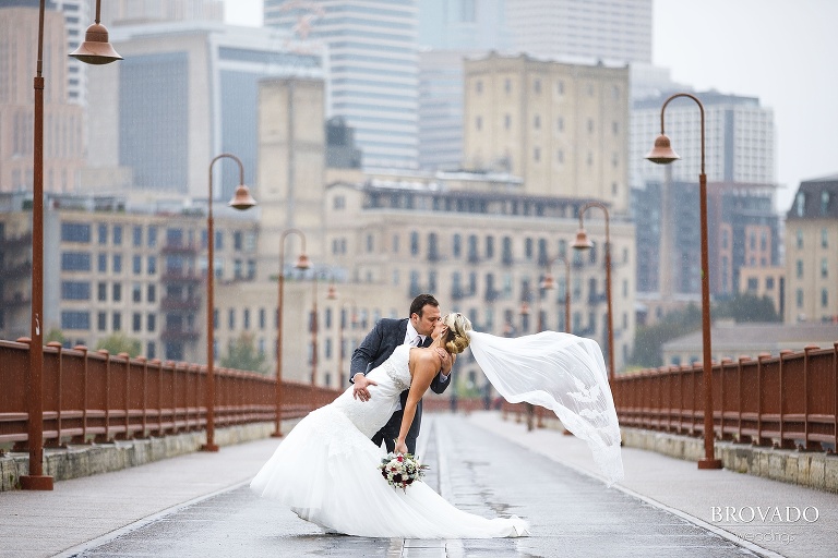 Rachel and Joe kissing and dipping in the rain on stone arch bridge