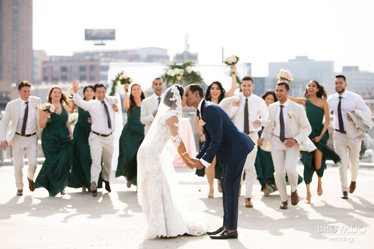Bride and groom kissing as wedding party runs towards them
