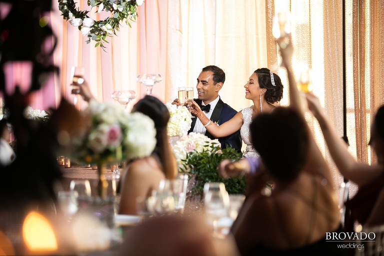 Bride and groom toasting in front of gold backdrop