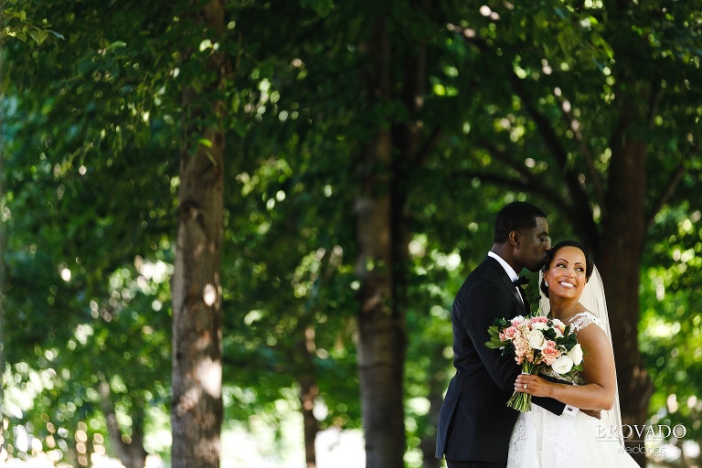 Groom kissing bride on her forehead while she looks over her shoulder