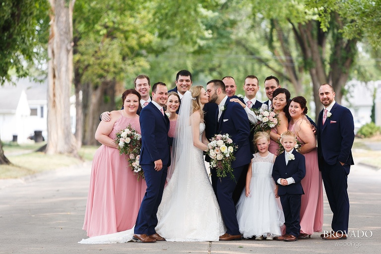 Wedding party huddled around kissing bride and groom