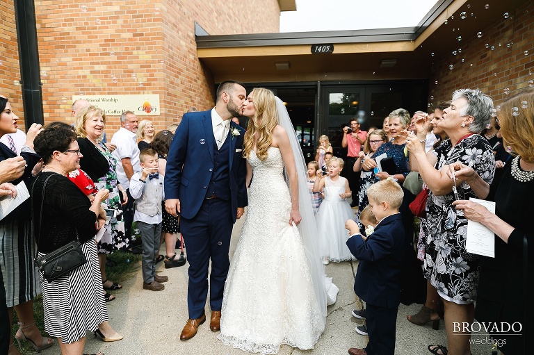 Bride and groom exit church while guests blow bubbles