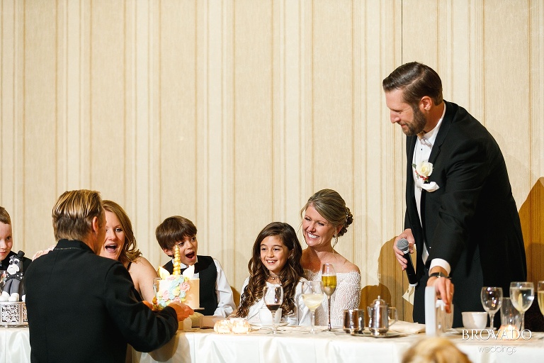 Bride and groom giving flower girl a unicorn birthday cake