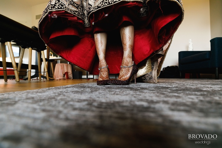 Closeup of bride's henna covered feet in maroon sparkly shoes