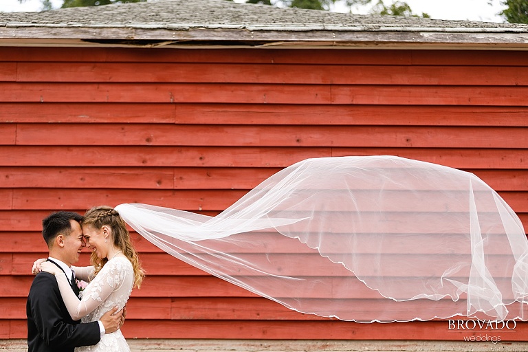 Bride and groom in front of red painted wall with flying veil