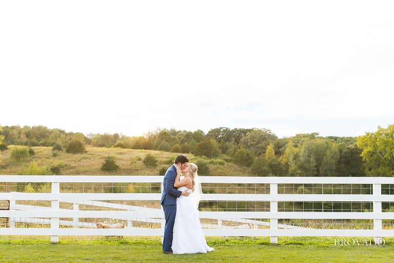 Bride and groom kissing in front of fence and goats at almquist farm