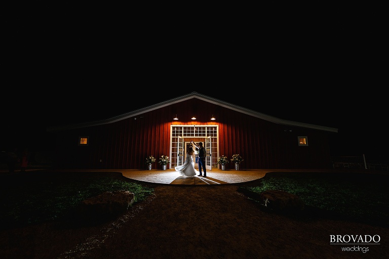 Groom twirling the bride in front of the barn in dramatic lighting