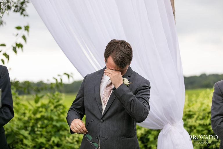 Groom wiping away tears while the bride walks down the aisle