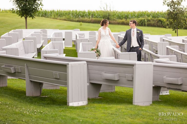 Heather and Daniel holding hands among outdoor wedding pews