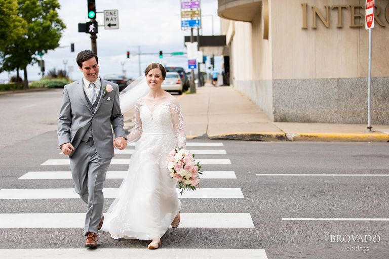 Smiling bride and groom running across the street in downtown St. Paul